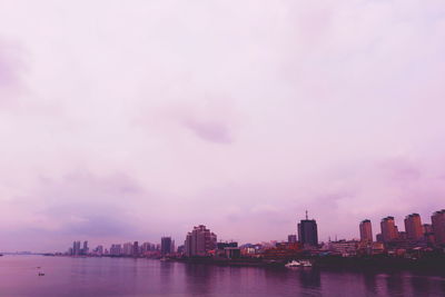 River by cityscape against sky during sunset