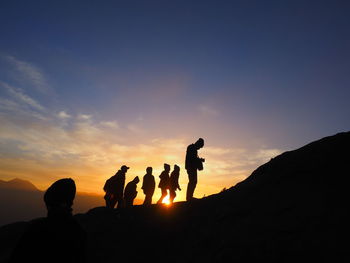 Silhouette people on rock against sky during sunset