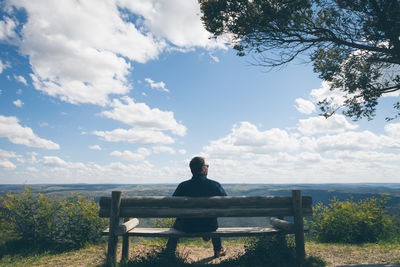 Rear view of man sitting on beach at field against sky