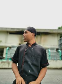 Young man looking away while standing against built structure