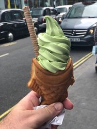 Hand holding ice cream cone on street in city
