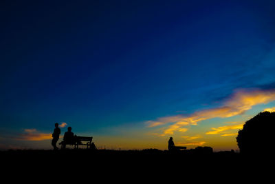 Silhouette people walking on field against sky during sunset