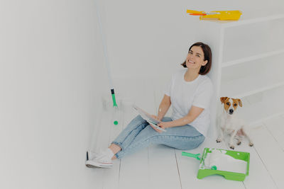 Full length of woman holding color swatch sitting on floor with dog at home