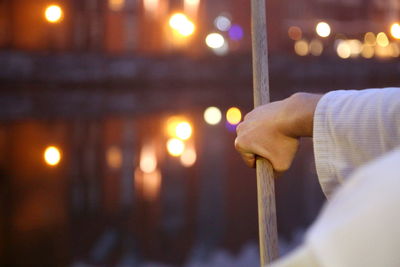 Cropped image of man practicing martial arts with sword against illuminated canal in city during sunset