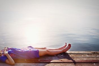 Low section of woman relaxing on wooden pier against water