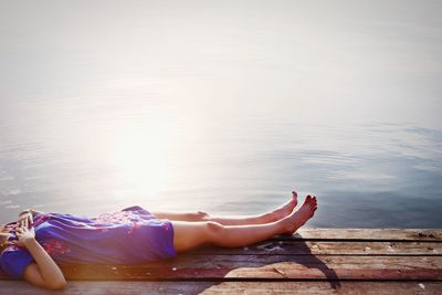 Low section of woman relaxing on wooden pier against water