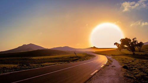 Country road against sky during sunset