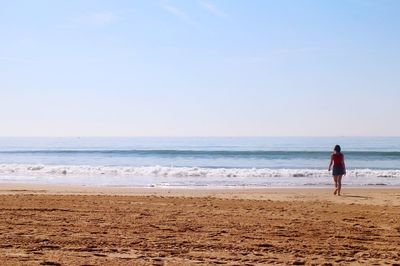 Rear view of woman walking at beach against sky