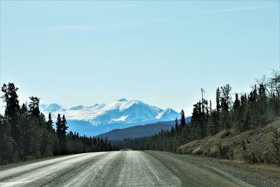 Road amidst trees and mountains against sky