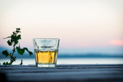 Beer glass on table against sea during sunset