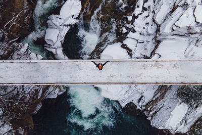 Aerial drone shot of the woman standing on the bridge through the mountain river. 