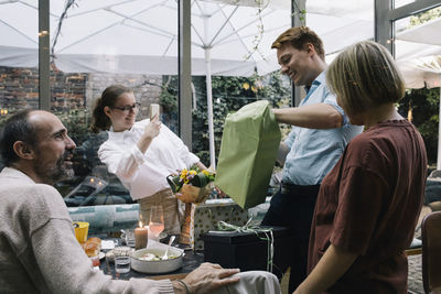 Smiling man unwrapping gift box during party