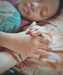 High angle view of girl holding cropped hand while sleeping on bed at home