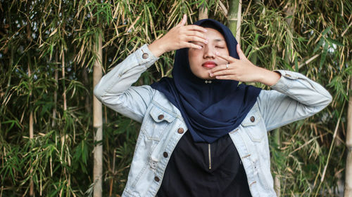 Thoughtful woman with eyes closed standing against bamboos