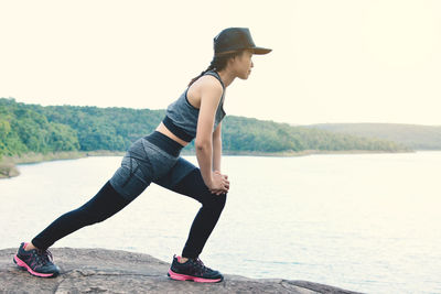 Side view of woman exercising on rock against lake