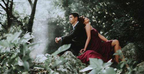 Woman sitting on plant against trees