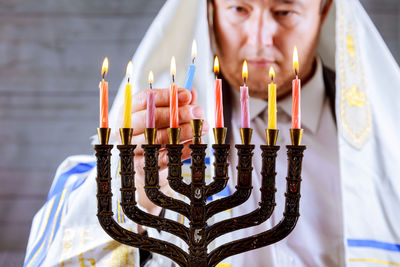 Mature man in jewish prayer shawl burning candles on hanukkah menorah