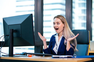Surprised young woman looking at computer in office