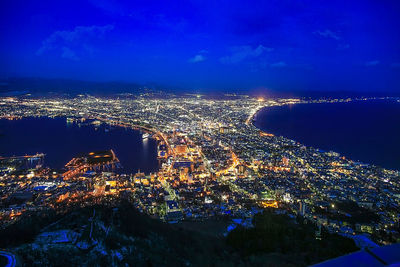 High angle view of illuminated city by sea against sky