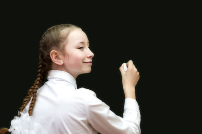 Rear view of girl holding chalk standing by blackboard