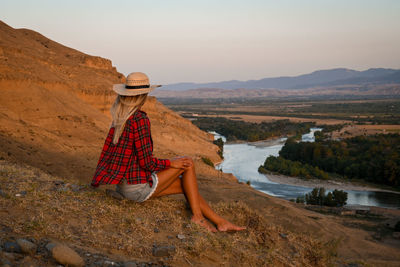 A girl sitting on the rock at sunset, arid landscape.