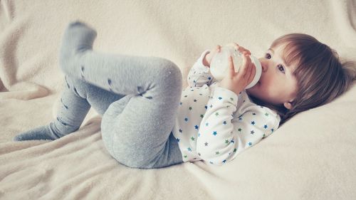 High angle view of girl drinking milk from bottle while lying on bed at home