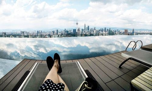 Low section of woman sitting on railing by sea against sky