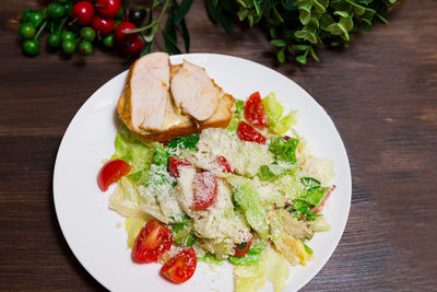 A plate of caesar salad view from above. iceberg lettuce, cherry tomatoes, parmesan, chicken fillet.