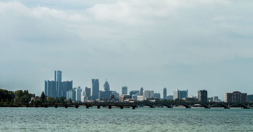 Scenic view of river by cityscape against sky