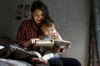 Happy woman with baby boy reading book at home