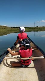 Rear view of children on boat in lake against sky