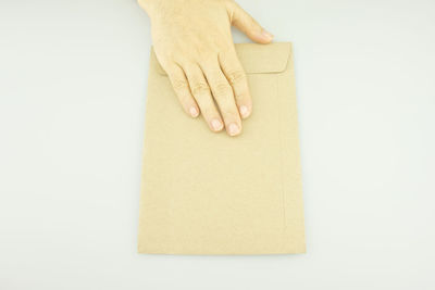 Close-up of hand touching envelope on white background