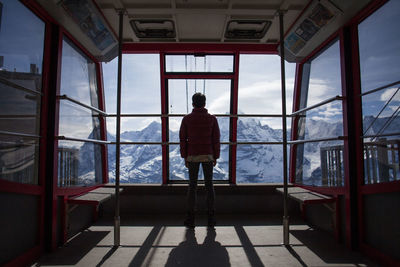 Rear view of person looking towards snowcapped mountains through ski lift windows