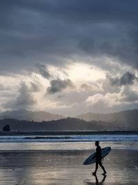 Rear view of woman standing at beach against sky during sunset