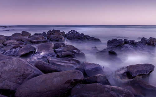 Rocks on beach against sky during sunset