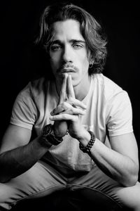 Portrait of young man sitting against black background