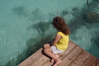 High angle view of girl sitting on pier over sea