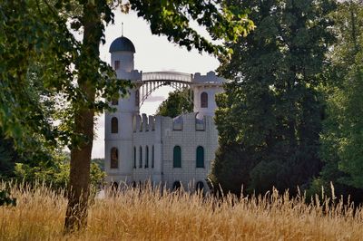 Historic building by trees on field against sky