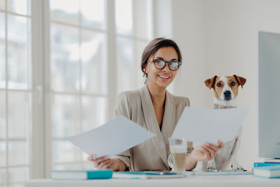 Portrait of young woman with dog sitting at desk in office