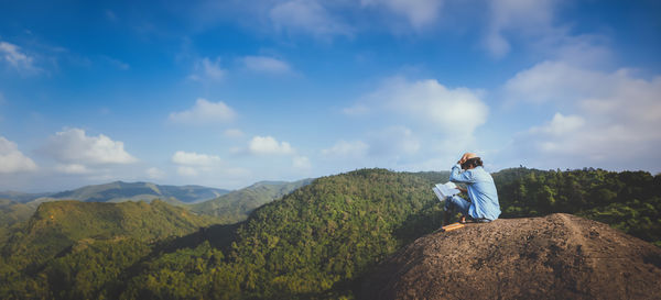 Rear view of woman sitting on mountain against sky