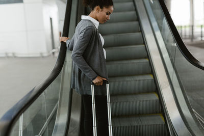 Side view of woman pulling luggage on escalator