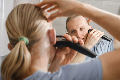 Personal hygiene, caucasian man cutting his own hair in the bathroom with wireless electric shaver