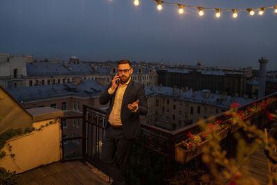 Businessman gesturing while talking on smart phone near railing during night