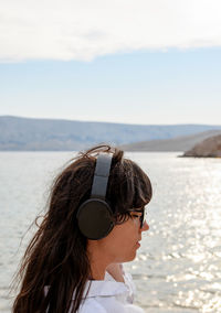 Beautiful young woman standing on beach listening to music on headphones.