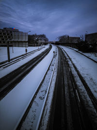 Railroad tracks by snow covered city against sky