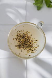 Healthy bone broth with spices in a mug on a white tile with a shadow pattern. top view.