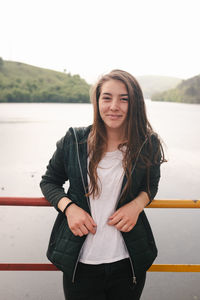 Portrait of beautiful young woman standing against lake