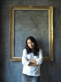 Portrait of woman with arms crossed standing against wall