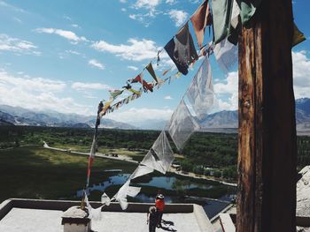 Prayer flags and people on building terrace by landscape against cloudy sky