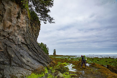 Man on rock by sea against sky